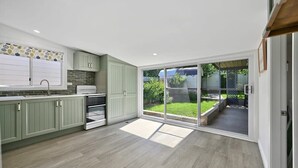A modern kitchen with green cabinets, a built-in oven, and a large sliding glass door leading to a backyard. - Autumn Leaf Cottage - Close to CBD, Heritage Charm (Orange)