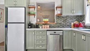 A kitchen with light green cabinets, a stainless steel dishwasher, and a white refrigerator. - Autumn Leaf Cottage - Close to CBD, Heritage Charm (Orange)