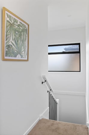 A staircase with a handrail, a window with a view of a ship, and a framed botanical print on the wall.