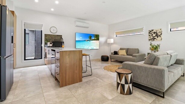 Ein modernes Wohnzimmer mit einem grauen Sofa, einem Holztisch und einem Fernseher, der eine Strandansicht zeigt.
