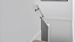 Eine Treppe mit weißer Geländer, ein gerahmtes Pflanzenbild und ein Fenster mit Blick auf ein Gewässer.