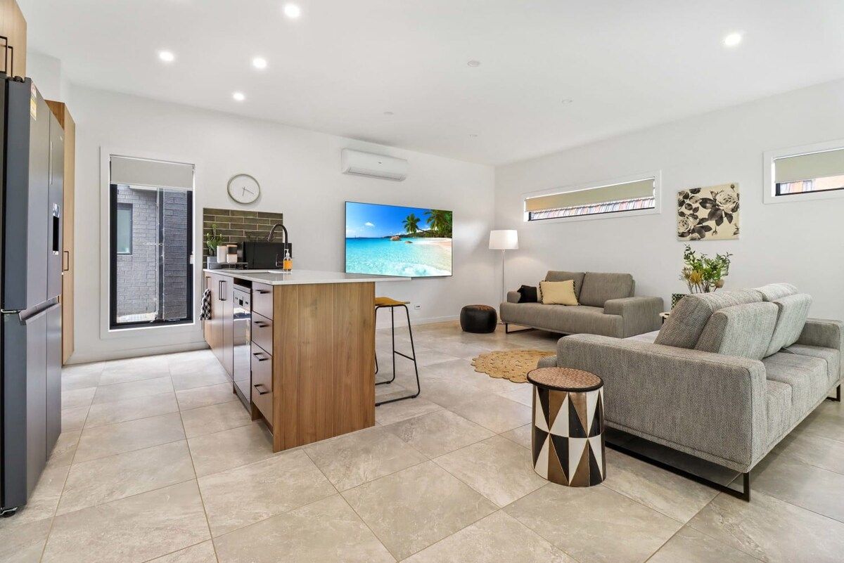A modern living room with a grey sofa, a wooden coffee table, and a TV mounted on the wall.