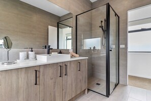 Un baño moderno con cabina de ducha de vidrio, un espejo grande y una encimera blanca con artículos de aseo.