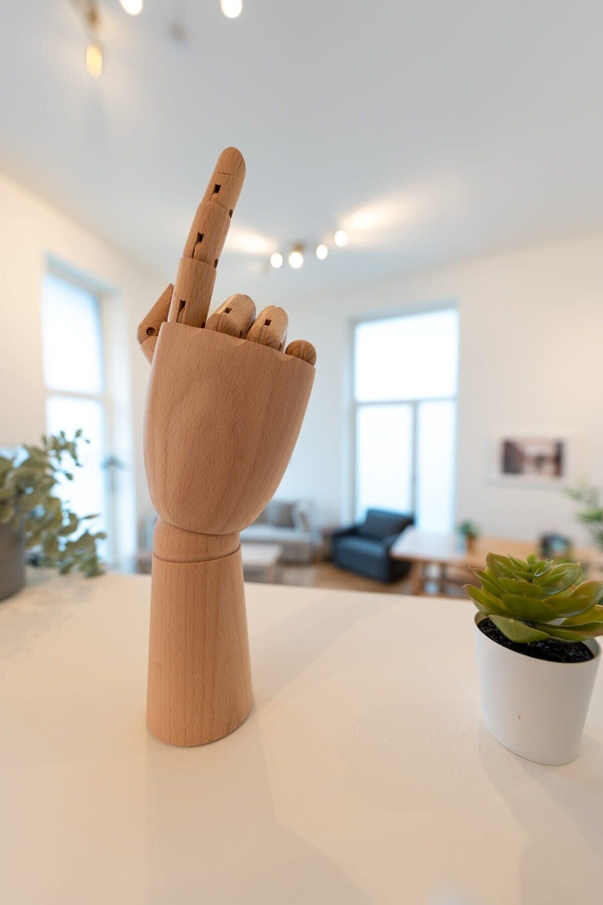 Eine Holzhandschulptur auf einem Tisch in einem modernen Raum mit großen Fenstern, einer Pflanze und einer Couch im Hintergrund.