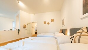 Ein Hotelzimmer mit drei Betten, Holzboden und einer weißen Wand mit kleinem Fenster.