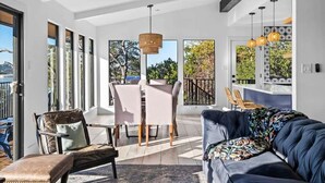A modern living room with a sofa, chairs, a dining table, and large windows. - Waterfront / Pool / Hot tub / Boat Dock (Leander)