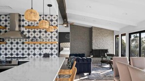 A modern kitchen with a large island, a dining area with wicker chairs, a stone fireplace, and a view of the outdoors. - Waterfront / Pool / Hot tub / Boat Dock (Leander)