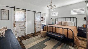 Een slaapkamer met een bed, een bankje, een dressoir, een kroonluchter en een muur met een citaat.
