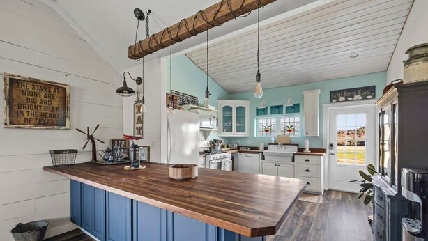Een keuken met een houten kookeiland, witte kasten en een spoelbak in boerderijstijl.