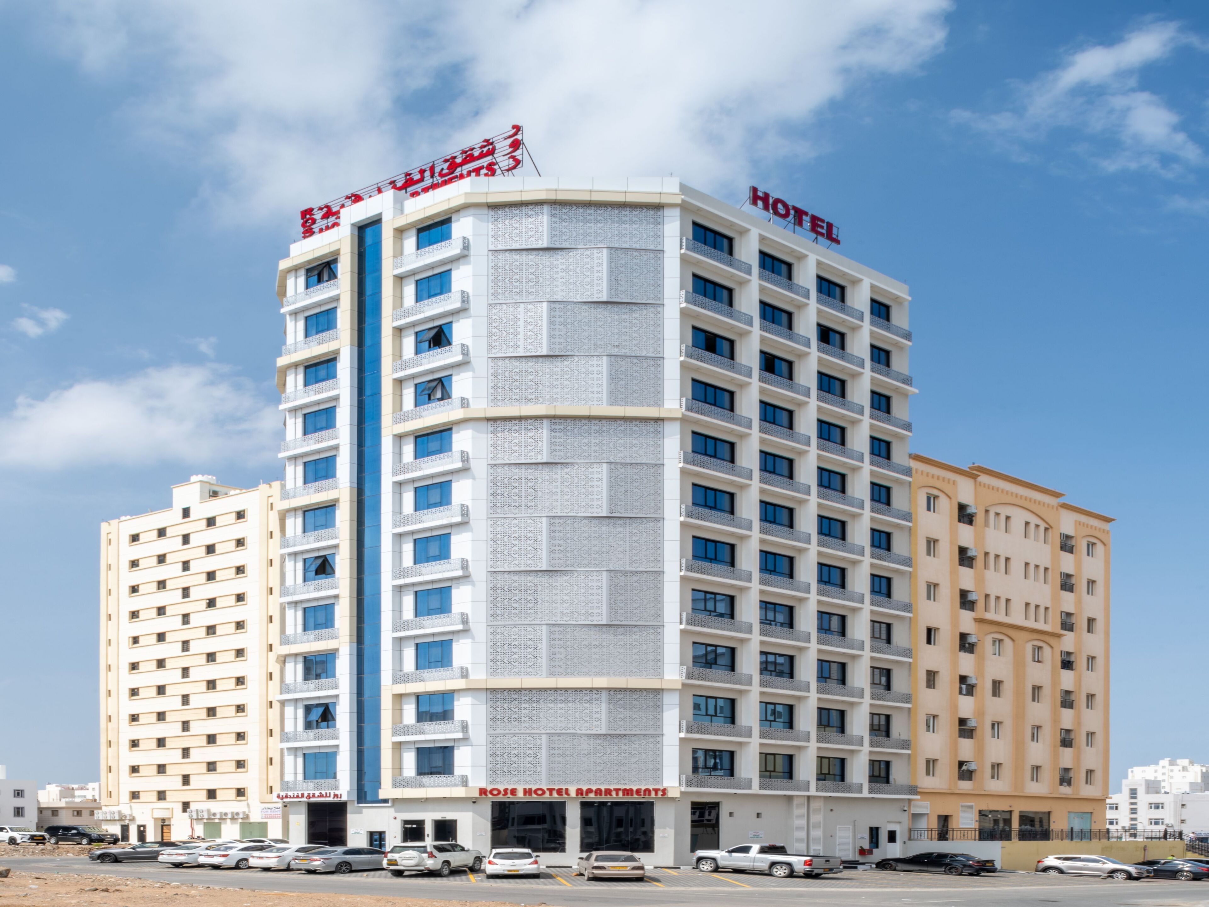 Een meerlaags hotel met een opvallend “HOTEL”-bord bovenop. Het gebouw heeft een modern design met een combinatie van witte en beige buitenmuren.