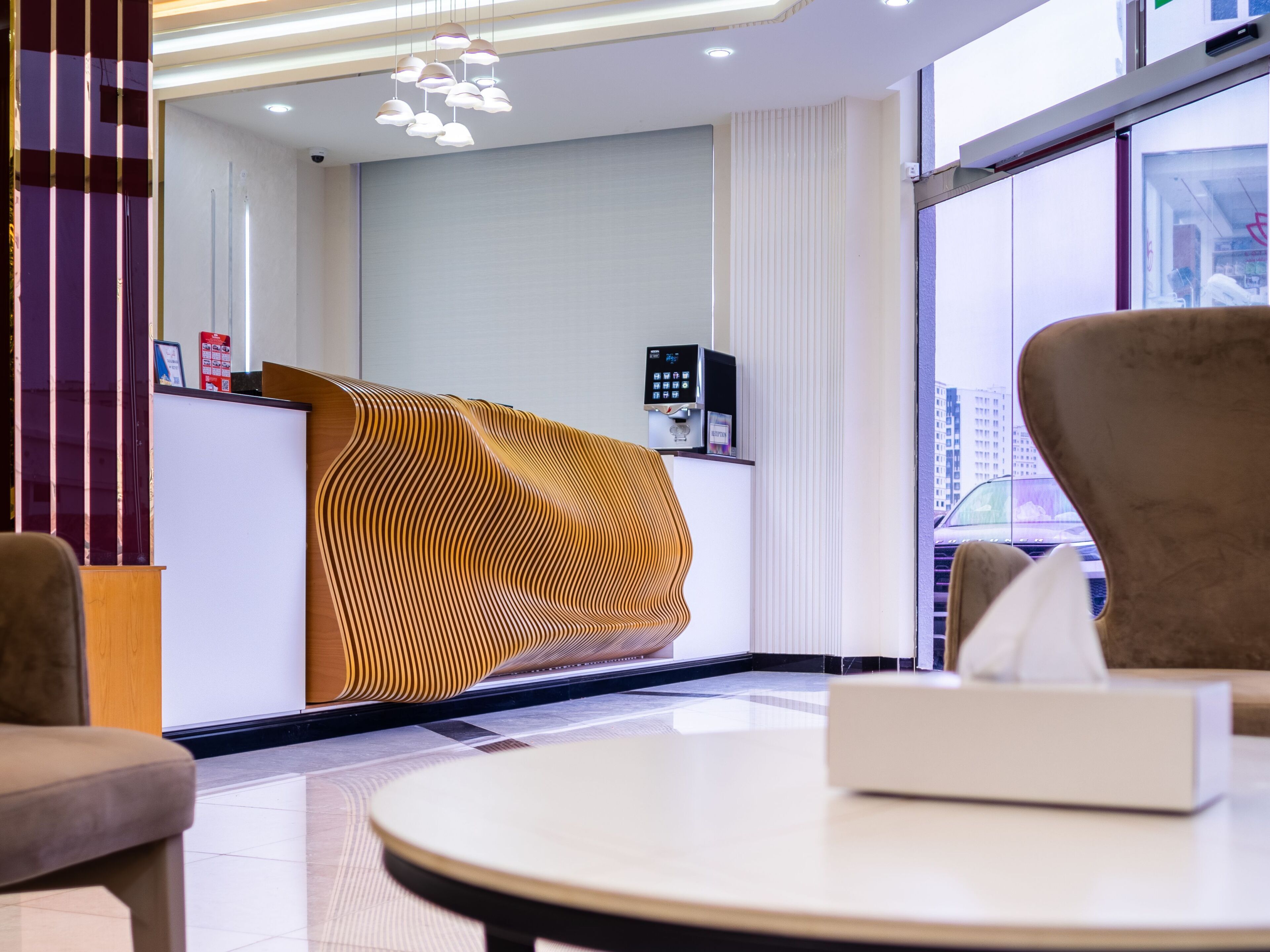 A modern hotel reception area with a unique wavy wooden reception desk, a digital check-in kiosk, and a view of the city through large windows.