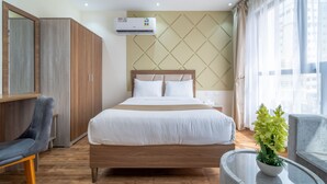 A modern hotel room with a wooden bed, a grey armchair, a small round table with a plant, and a ceiling fan. - OYO Townhouse 156 Rose Hotel Apartments. (Seeb)