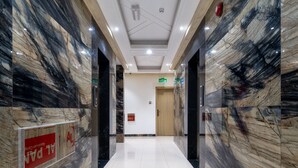 A modern hallway with marble walls and a polished floor, leading to an exit door. - OYO Townhouse 156 Rose Hotel Apartments. (Seeb)