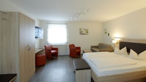 A hotel room with a bed, a desk, two chairs, a sofa, and a TV.