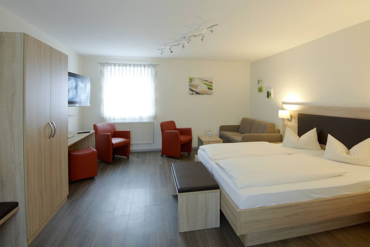 Ein Hotelzimmer mit einem Bett, einem Schreibtisch, zwei Stühlen, einem Sofa und einem Fernseher.