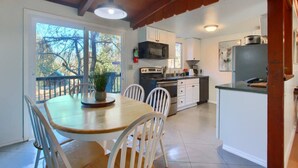 Une cuisine avec des meubles blancs, un four à micro-ondes et une cuisinière. On y trouve une table à manger avec des chaises et une plante en pot.