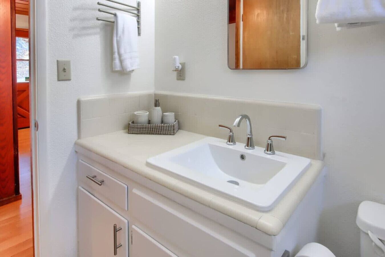 Une salle de bain avec un lavabo blanc, deux robinets, un miroir et un porte-serviettes.