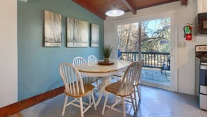 Un coin repas avec une table ronde et des chaises blanches, un ventilateur de plafond et une vue sur l’extérieur grâce à une porte-fenêtre coulissante.