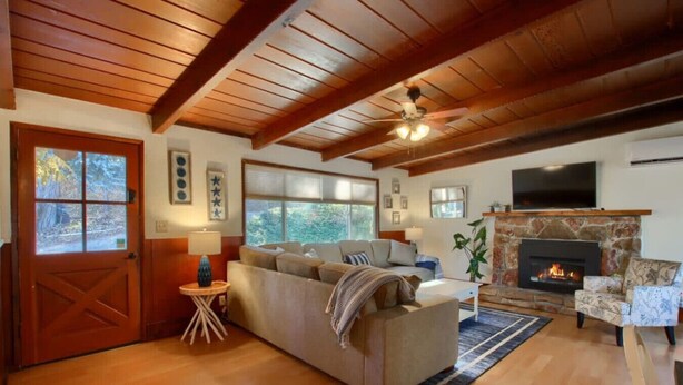 Un salon chaleureux avec une cheminée, des poutres apparentes en bois et une grande fenêtre.