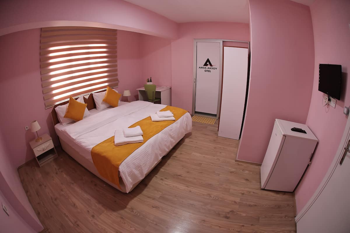 A pink-themed hotel room with a bed, bedside table, lamp, and a wardrobe.