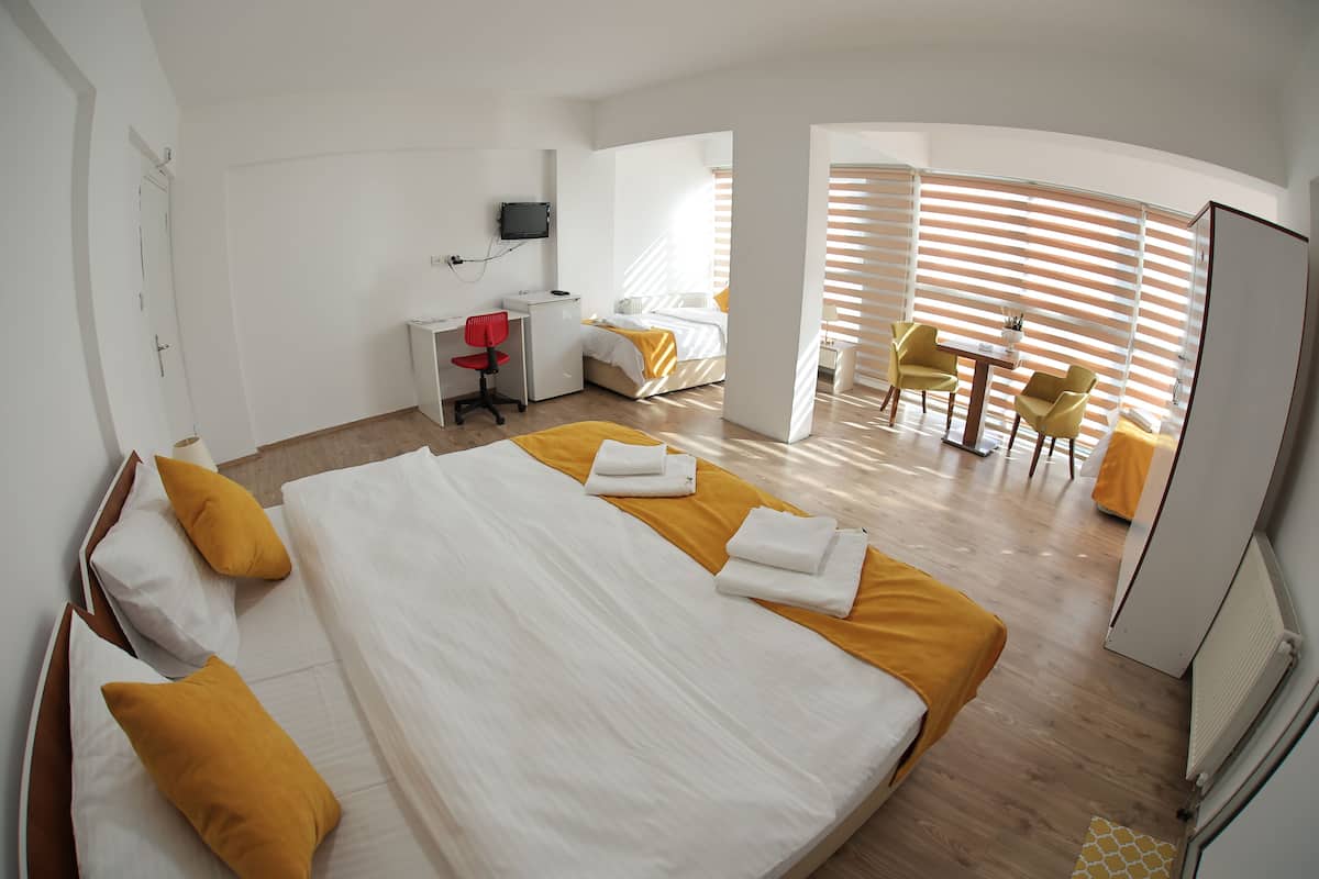 A hotel room with a large bed, a desk, a chair, and a dining area with a table and chairs.