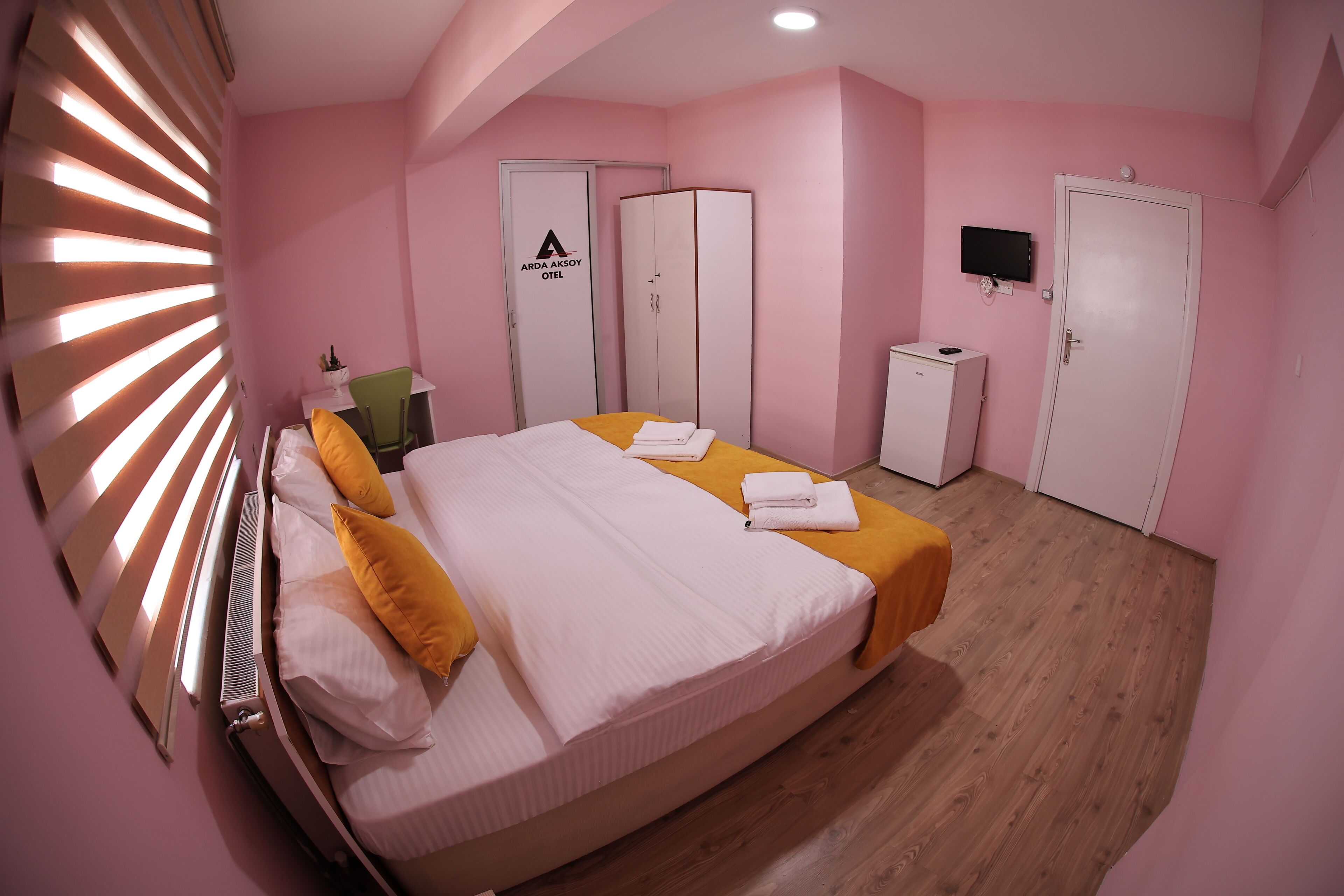 A pink-themed hotel room with a bed, a wardrobe, a desk, and a television.