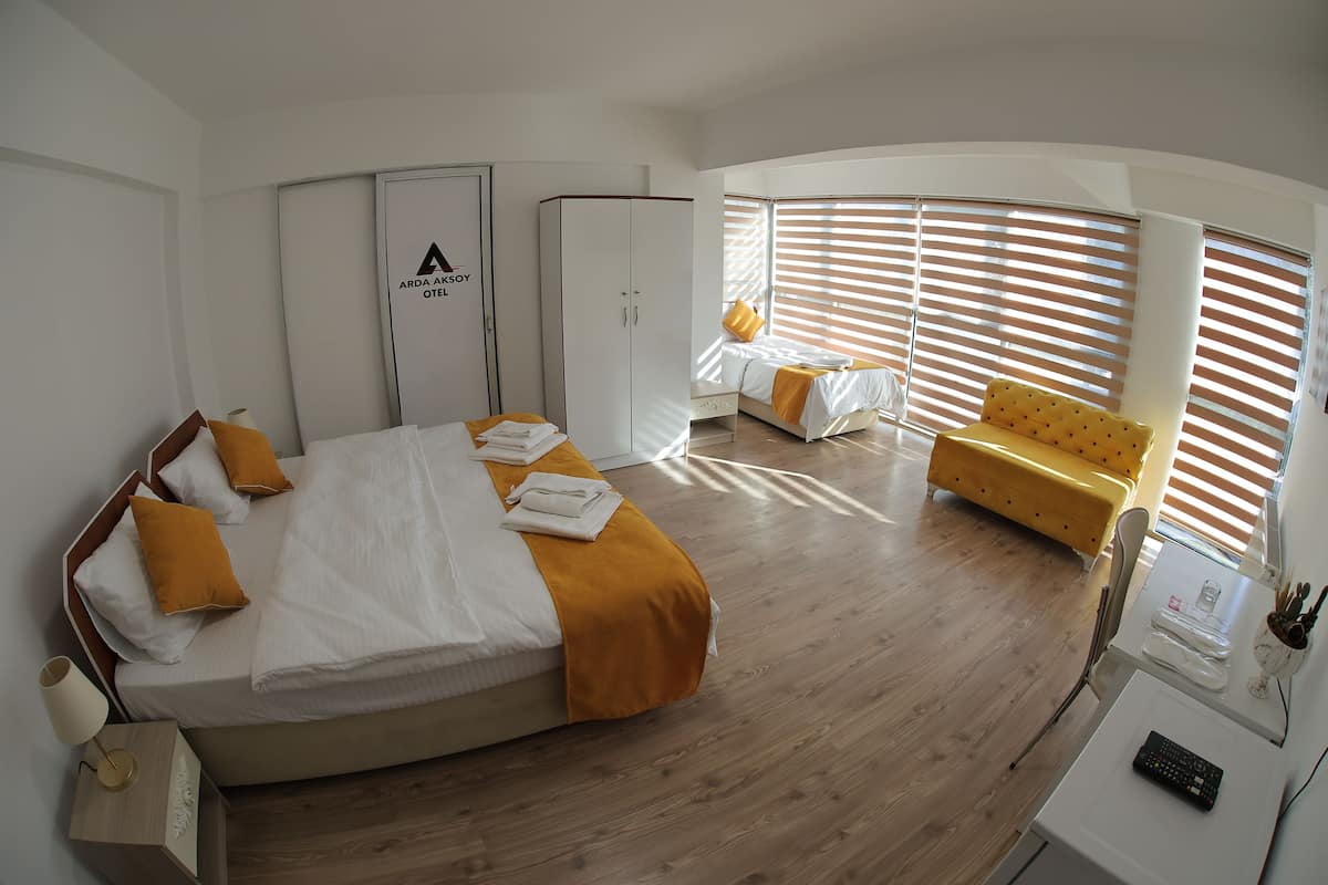 A modern hotel room with a large bed, a yellow sofa, and a desk with a keyboard.
