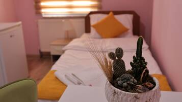 Quarto com cama, mesa de cabeceira com uma planta de cacto e janela com persianas.