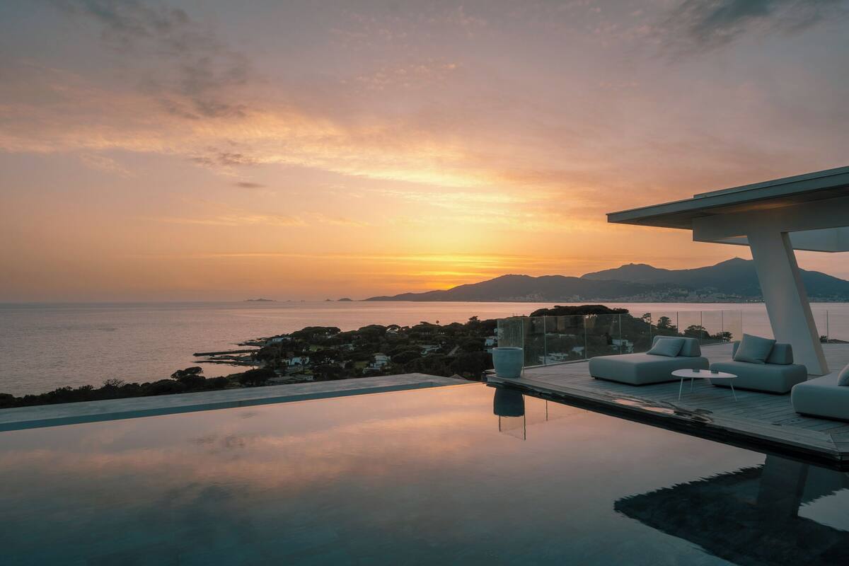 An infinity pool with a sunset view, outdoor seating, and a modern architectural design.