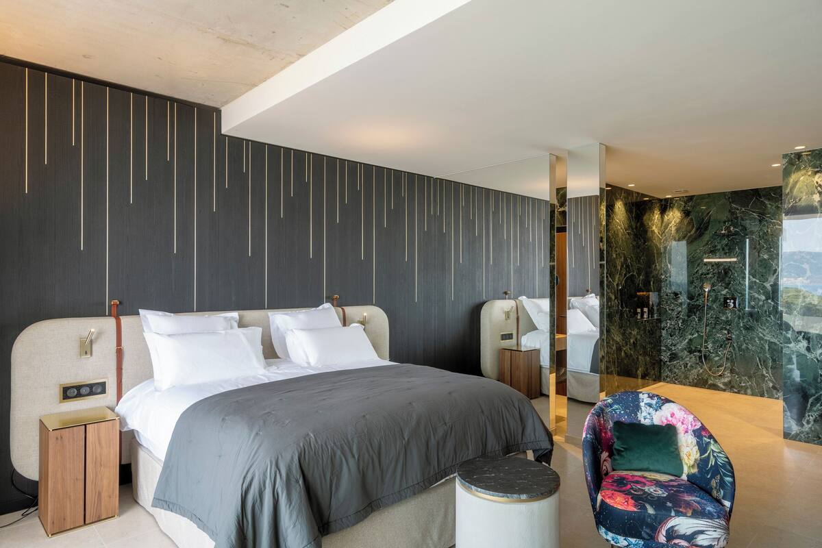 A modern hotel room with a large bed, a small side table, a chair, and a bathroom with a marble wall.