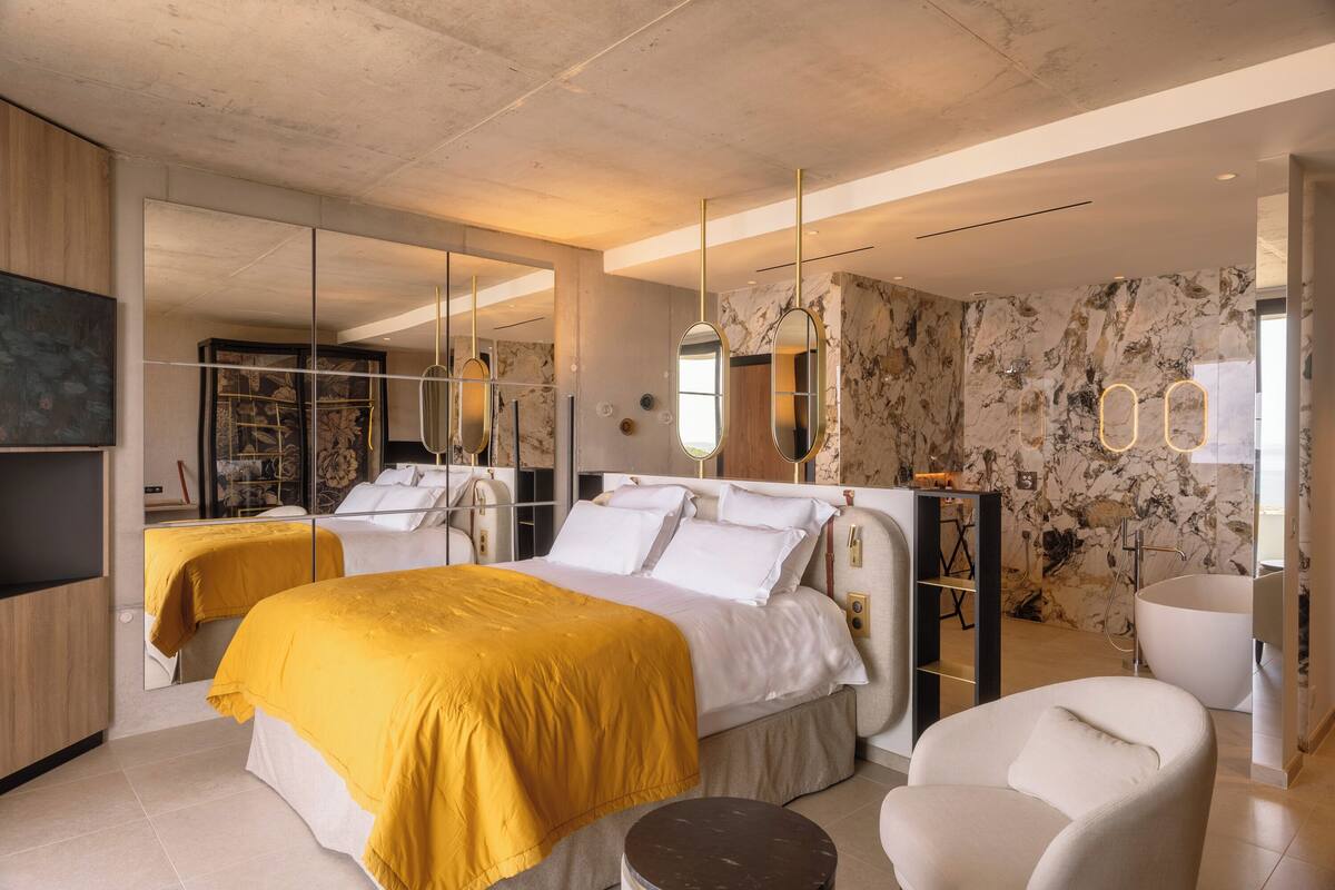 A modern bedroom with a large bed, a sitting area, and a bathroom with a bathtub.