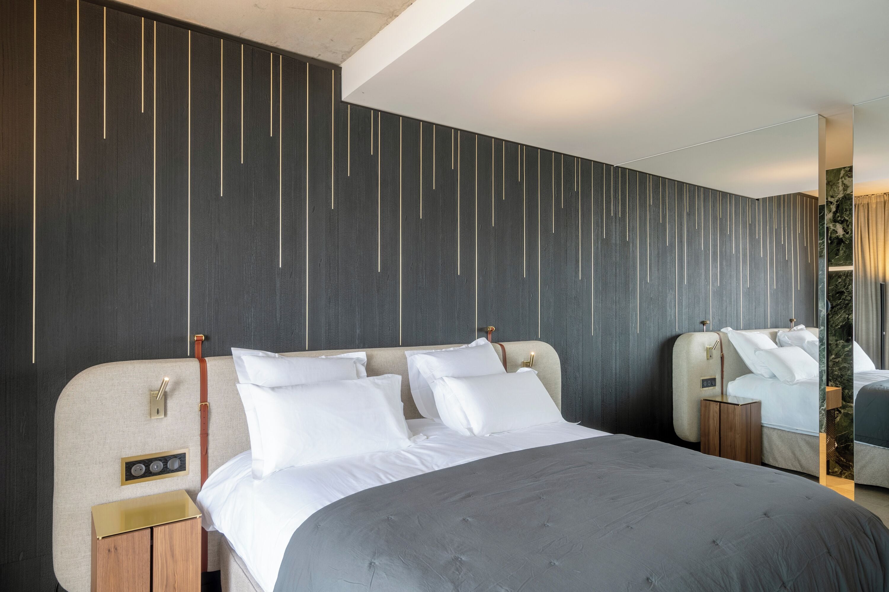 Ett modernt hotellrum med en stor säng, ett sängbord och en spegel.