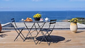 Une table entourée de chaises et une plante en pot, le tout placé sur une terrasse en bois donnant sur la mer.
