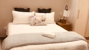 A neatly made bed with white bedding and a single pillow, a bedside lamp, and a wooden nightstand. - Premier Lifestyle at The Regency (Pretoria)