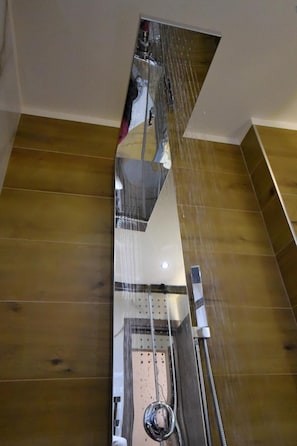 A modern bathroom with a large mirror, a shower with a glass enclosure, and wooden flooring.
