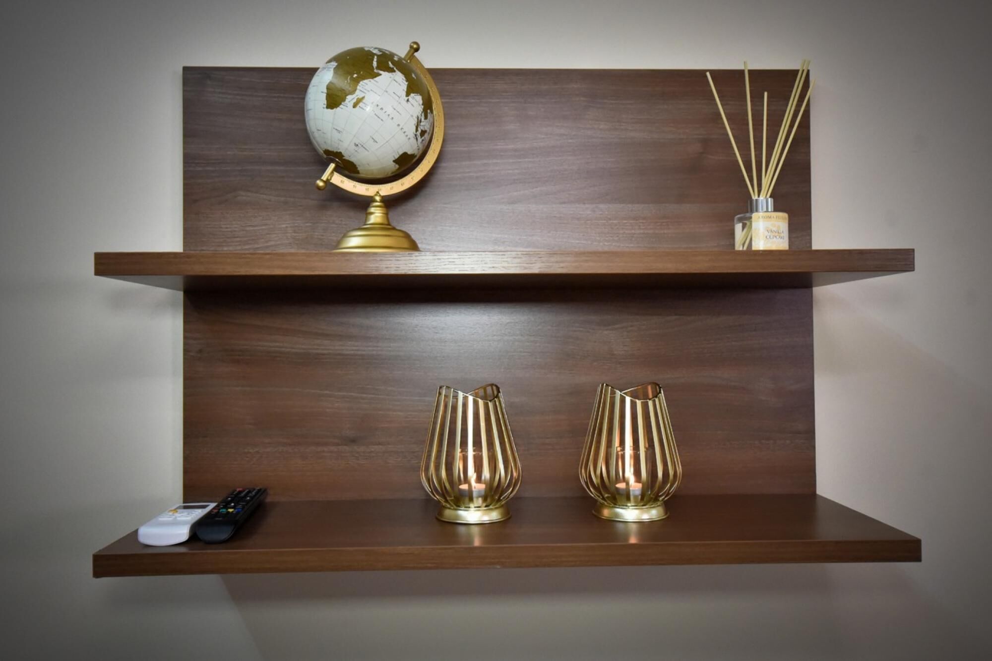 A shelf with a globe, two candle holders, a reed diffuser, and a remote control.