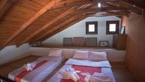 A small, cozy attic bedroom with two beds, wooden beams, and a view of the outside.