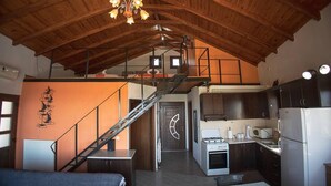 A rustic interior with a loft bedroom, kitchen, and staircase.