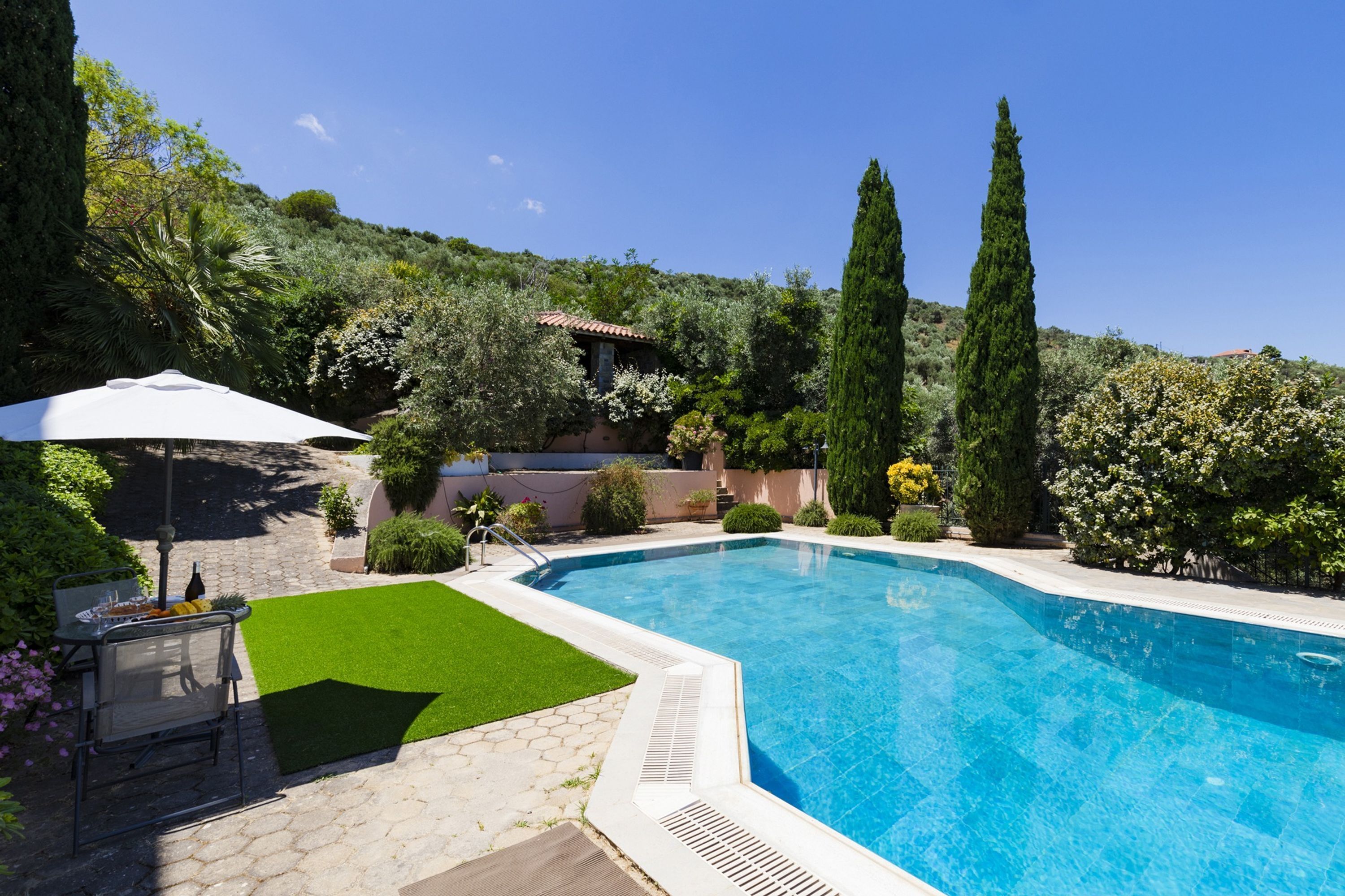 A swimming pool surrounded by lush greenery and a patio area with outdoor furniture.