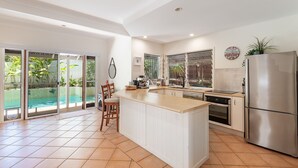 A modern kitchen with a large island, a built-in oven, and a refrigerator. There is a sliding glass door leading to a pool area. - Comfortable Family Townhouse, Sunrise Beach (Sunrise Beach)