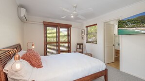 A bedroom with a bed, a ceiling fan, wooden shutters, a TV, and a view of a beach through an open door. - Comfortable Family Townhouse, Sunrise Beach (Sunrise Beach)