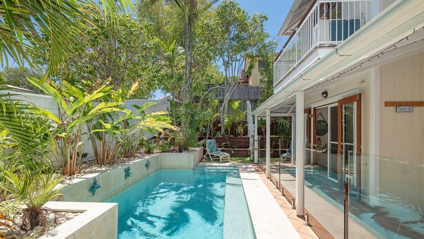 A swimming pool with a glass enclosure, surrounded by tropical plants and a wooden deck. - Comfortable Family Townhouse, Sunrise Beach (Sunrise Beach)