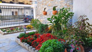 A courtyard with a variety of potted plants and flowers, a stone wall, and a metal fence. - Alexia s Residence in Volos (Volos)