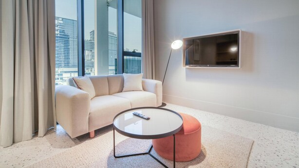 A modern living room with a sofa, a round coffee table, and a television on the wall. - Modern Studio Apt w Burj Khalifa View (Dubai)