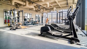A gym with exercise equipment, large windows, and a high ceiling. - Modern Studio Apt w Burj Khalifa View (Dubai)