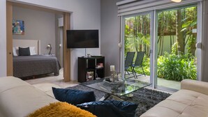 Una sala moderna con una cama, un televisor de pantalla plana, una mesa de centro de vidrio y un ventanal corredero que da a un jardín.