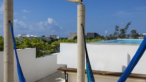 Una hamaca bajo una zona con sombra, con vista a una piscina y edificios al fondo.