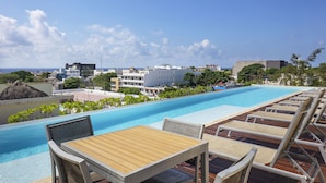 Zona de piscina en la azotea con sillones de descanso y una mesa, con vistas a la ciudad y al océano.