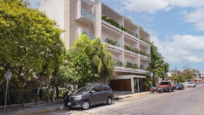 Un edificio de varios pisos con balcones, vista a la calle y vehículos estacionados.