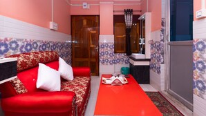 A compact living space with a red sofa, a small dining table, and a kitchen area with a window. - RAJA HOTEL AND LODGE  (Kharagpur)